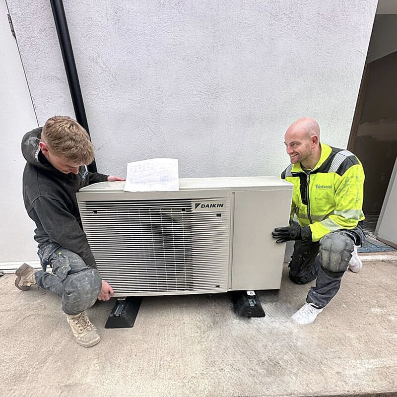 two males placing an air source heat pump into position beside a residential property in Yorkshire